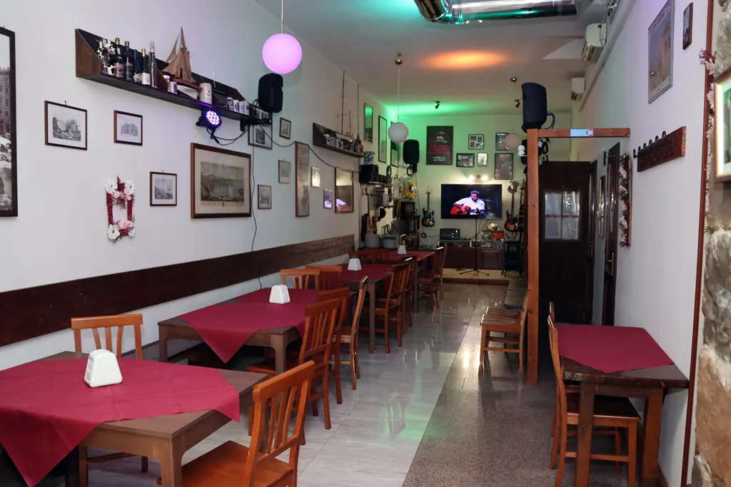 La sala del buffet di giorno: file di tavoli con tovaglie bordeaux, sedie in legno e cornici alle pareti