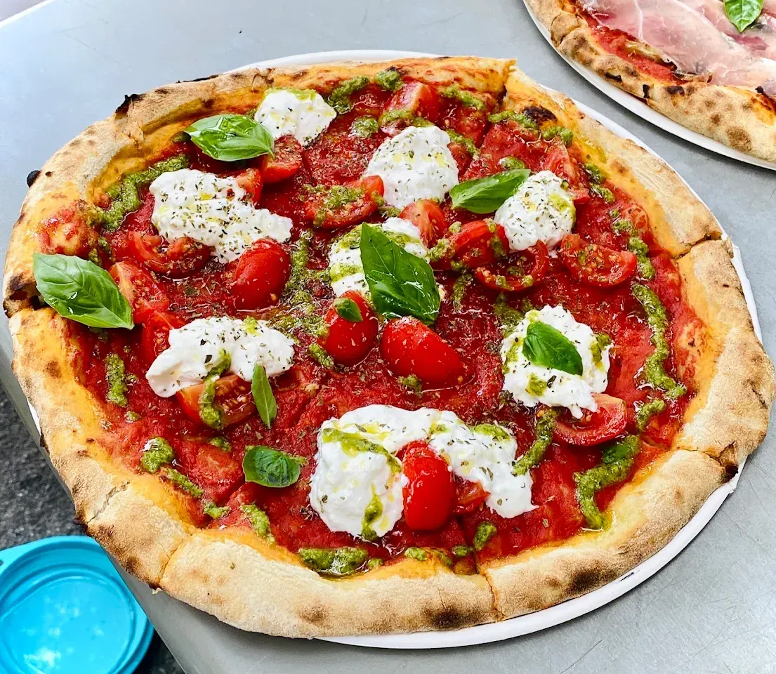 Pizza rossa con pomodorini, stracciatella, pesto e basilico